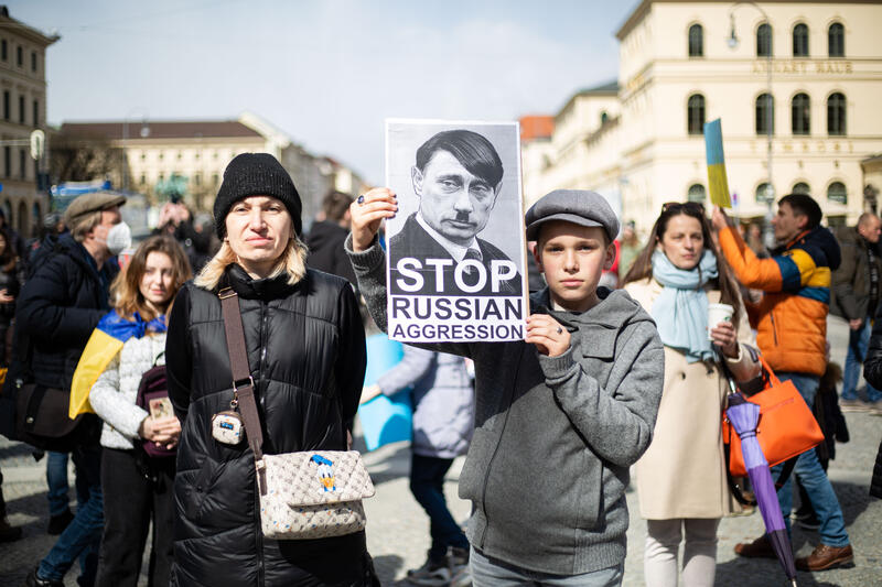 Junge mit Schild mit Putin als Hitler: " Stop Russain Aggression ". Am 9. April 2022 versammelten sich in München zahlreiche Menschen, um nach dem brutalen Massaker von Bucha gegen den russichen Krieg gegen die Ukraine zu demonstrieren.   *   Boy with sign showing Putin as Hitler reads: " Stop Russain Aggression ". On April 9, 2022 thousand people gathered in Munich, Germany to protest against the Russian invasion in Ukraine and remebered of the dead of the massacre of Bucha.