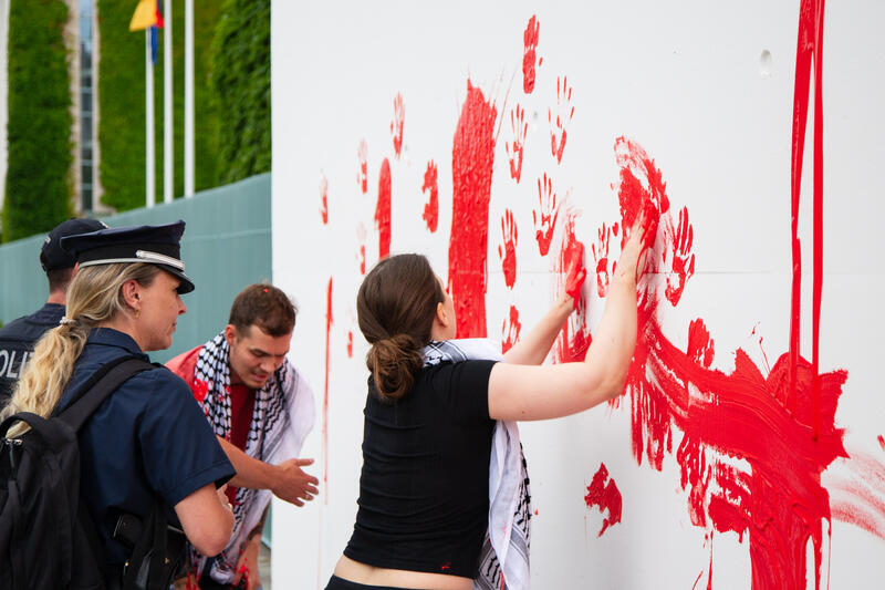 Am 07.07.2025 um 12 Uhr beschmierten Aktivist*innen von Palestine Rising die rechte Seite der Fassade des Bundeskanzleramtes in Berlin, Deutschland. Sie hinterließen rote Handabdrücke an der Wand. Sie demonstrieren damit gegen die deutsche Unterstützung von Kriegsverbrechen in Gaza.   --    On July 7, 2025 activists from Palestine Rising, a group of the New Generation, smeared the facade of the federal chancellery in Berlin, Germany with red paint. They left red hand prints at the wall. With their action the activists protest against German support for the Israeli war crimes in Gaza.