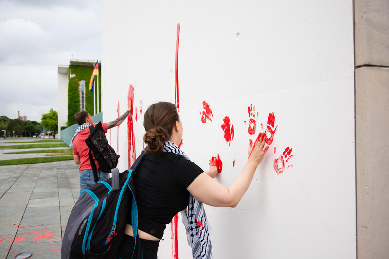Am 07.07.2025 um 12 Uhr beschmierten Aktivist*innen von Palestine Rising die rechte Seite der Fassade des Bundeskanzleramtes in Berlin, Deutschland. Sie hinterließen rote Handabdrücke an der Wand. Sie demonstrieren damit gegen die deutsche Unterstützung von Kriegsverbrechen in Gaza.   --    On July 7, 2025 activists from Palestine Rising, a group of the New Generation, smeared the facade of the federal chancellery in Berlin, Germany with red paint. They left red hand prints at the wall. With their action the activists protest against German support for the Israeli war crimes in Gaza.