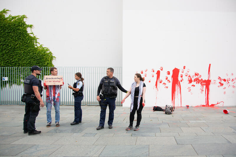 Am 07.07.2025 um 12 Uhr beschmierten Aktivist*innen von Palestine Rising die rechte Seite der Fassade des Bundeskanzleramtes in Berlin, Deutschland. Sie hinterließen rote Handabdrücke an der Wand. Sie demonstrieren damit gegen die deutsche Unterstützung von Kriegsverbrechen in Gaza.   --    On July 7, 2025 activists from Palestine Rising, a group of the New Generation, smeared the facade of the federal chancellery in Berlin, Germany with red paint. They left red hand prints at the wall. With their action the activists protest against German support for the Israeli war crimes in Gaza.