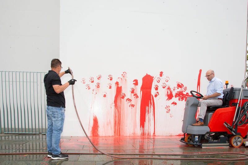 Reinigungsteam säubern die Stelle. Am 07.07.2025 um 12 Uhr beschmierten Aktivist*innen von Palestine Rising die rechte Seite der Fassade des Bundeskanzleramtes in Berlin, Deutschland. Sie hinterließen rote Handabdrücke an der Wand. Sie demonstrieren damit gegen die deutsche Unterstützung von Kriegsverbrechen in Gaza.   --    Cleaning team cleans the wall after the action. On July 7, 2025 activists from Palestine Rising, a group of the New Generation, smeared the facade of the federal chancellery in Berlin, Germany with red paint. They left red hand prints at the wall. With their action the activists protest against German support for the Israeli war crimes in Gaza.