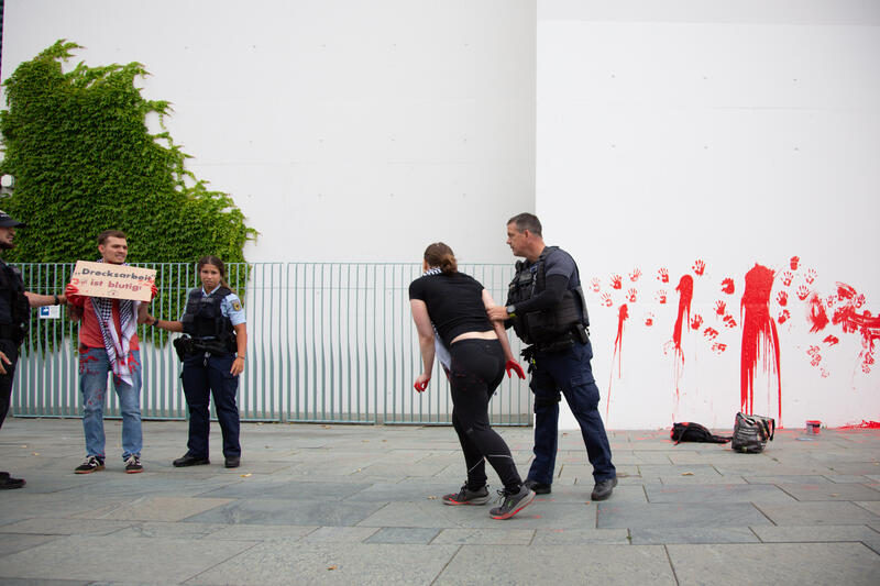 Am 07.07.2025 um 12 Uhr beschmierten Aktivist*innen von Palestine Rising die rechte Seite der Fassade des Bundeskanzleramtes in Berlin, Deutschland. Sie hinterließen rote Handabdrücke an der Wand. Sie demonstrieren damit gegen die deutsche Unterstützung von Kriegsverbrechen in Gaza.   --    On July 7, 2025 activists from Palestine Rising, a group of the New Generation, smeared the facade of the federal chancellery in Berlin, Germany with red paint. They left red hand prints at the wall. With their action the activists protest against German support for the Israeli war crimes in Gaza.