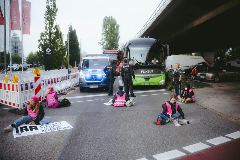 Am Morgen des 9. September 2025 blockierten Aktivist*innen des Widerstandskollektivs die Landshuter Allee in München, Deutschland, vor dem Mercedes Showroom, um gegen die IAA (Internationale Automobil-Ausstellung) zu protestieren.
Einige saßen dabei nur auf der Straße, andere klebten oder betonierten sich fest. Die festbetonierte Aktivist*in musste mit Hilfe einer Flex gelöst werden. --   On the morning of September 9, 2025, activists from the Resistance Collective blocked Landshuter Allee in Munich, Germany, in front of the Mercedes showroom to protest against the IAA (International Motor Show).
Some just sat on the street, others stuck or concreted themselves down.
The concreted activist had to be loosened with the help of an angle grinder.