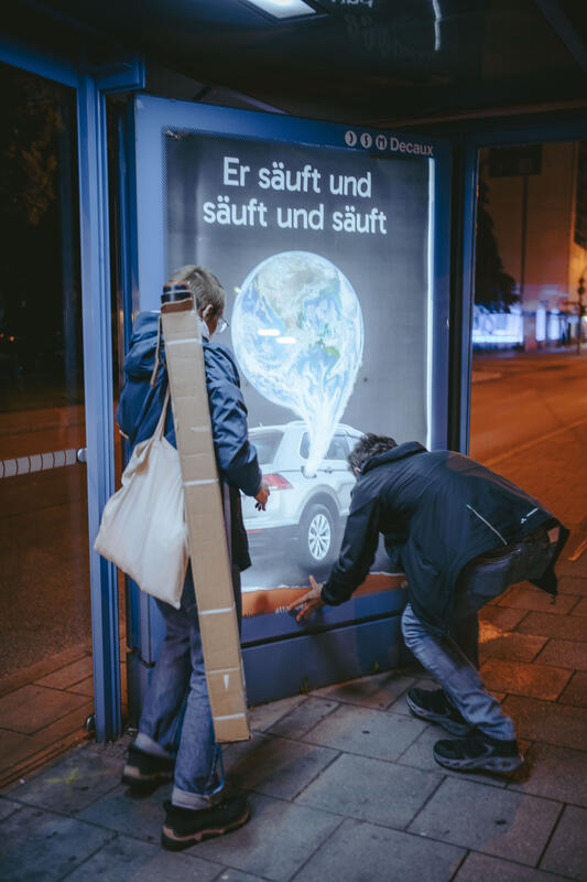 In der Nacht auf den 10.09.2025 versuchten zwei Aktivist:innen von Attac eine Adbusting-Aktion. Sie entfernten einige Werbeplakate und wollten sie durch Plakate gegen die IAA ersetzen. Da sie unvorbereitet waren, konnten sie einige Werbekästen nicht öffnen, einige konnten sie hingegen öffnen, aber ihre Plakate nicht aufhängen. Der Protest von Attac gegen die IAA begleiten sie mit der Froderung, nach einer sozial-ökologischen Wende in der Automobilindustrie und im gesamten Wirtschaftssystem. Sie fordern: Weniger Autos, und stattdessen mehr Platz für Fahrräder und Fußwege. -- On the night of September 10, 2025, two Attac activists attempted an adbusting campaign. They removed several advertising posters and wanted to replace them with posters against the IAA. Since they were unprepared, they were unable to open some of the advertising boxes, while others they were able to open but could not hang their posters. Attac's protest against the IAA is accompanied by demands for a socio-ecological transformation of the automotive industry and the entire economic system. They are calling for fewer cars and more space for bicycles and footpaths instead.
