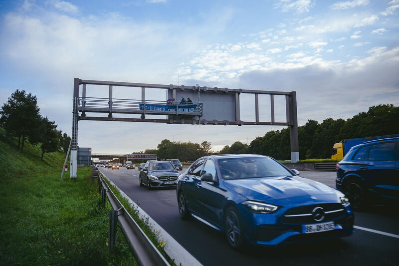 Am 11. September 2025, kurz nach 8, steigen drei Aktivist*innen auf eine Schilderbrücke über der Autobahn nahe der Allianz-Arena in München, Deutschland.
Dazu setzen sich wenig später 6 weitere Aktivist*innen auf die mittlerweile gesperrte Autobahn und kleben sich teilweise fest.
Auch zwei der Aktivist*innen auf der Brücke klebten sich fest, dies verzögerte die Räumung um einiges. Die Aktivist*innen gehörten dem Widerstandskollektiv an und protestierten mit dieser Aktion gegen die IAA, die zurzeit in München stattfindet.  -- On September 11, 2025, shortly after 8 a.m., three activists climb onto a sign bridge above the highway near the Allianz Arena in Munich, Germany.
A little later, six more activists sit down on the now closed highway and partially glue themselves to the ground.
Two of the activists on the bridge also glued themselves to the bridge, which delayed the evacuation considerably. The activists belonged to the resistance collective and were protesting against the IAA, which is currently taking place in Munich.