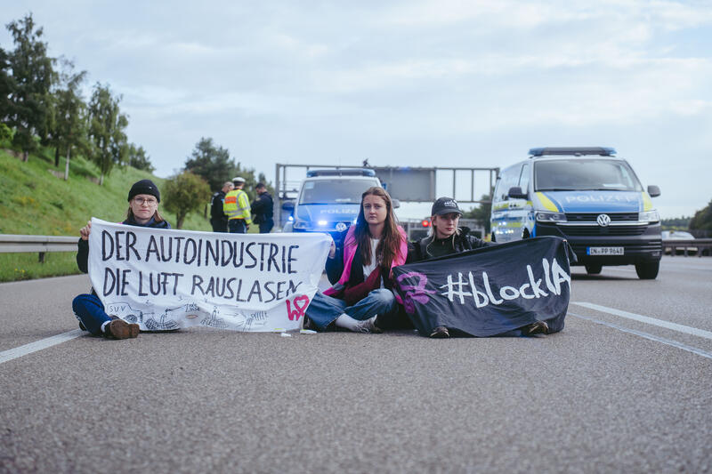 Am 11. September 2025, kurz nach 8, steigen drei Aktivist*innen auf eine Schilderbrücke über der Autobahn nahe der Allianz-Arena in München, Deutschland.
Dazu setzen sich wenig später 6 weitere Aktivist*innen auf die mittlerweile gesperrte Autobahn und kleben sich teilweise fest.
Auch zwei der Aktivist*innen auf der Brücke klebten sich fest, dies verzögerte die Räumung um einiges. Die Aktivist*innen gehörten dem Widerstandskollektiv an und protestierten mit dieser Aktion gegen die IAA, die zurzeit in München stattfindet.  -- On September 11, 2025, shortly after 8 a.m., three activists climb onto a sign bridge above the highway near the Allianz Arena in Munich, Germany.
A little later, six more activists sit down on the now closed highway and partially glue themselves to the ground.
Two of the activists on the bridge also glued themselves to the bridge, which delayed the evacuation considerably. The activists belonged to the resistance collective and were protesting against the IAA, which is currently taking place in Munich.