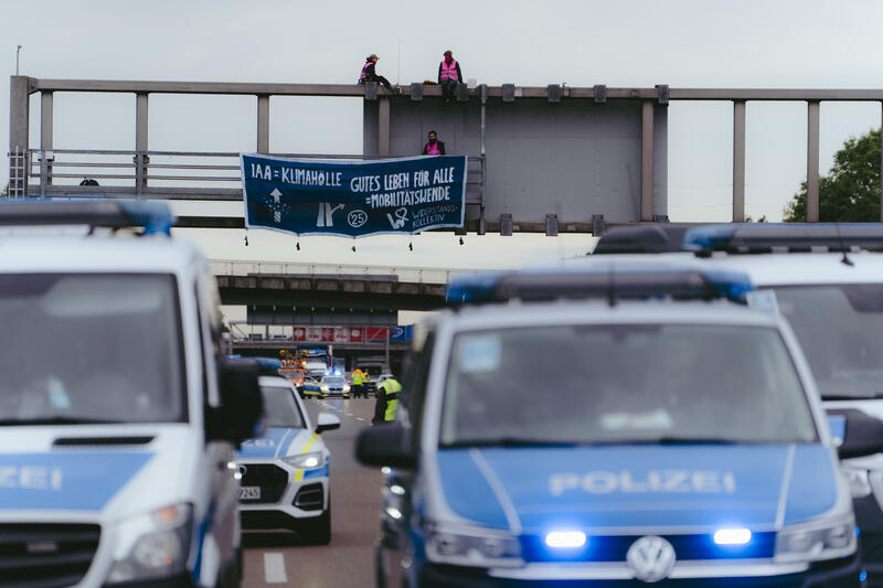 Am 11. September 2025, kurz nach 8, steigen drei Aktivist*innen auf eine Schilderbrücke über der Autobahn nahe der Allianz-Arena in München, Deutschland.
Dazu setzen sich wenig später 6 weitere Aktivist*innen auf die mittlerweile gesperrte Autobahn und kleben sich teilweise fest.
Auch zwei der Aktivist*innen auf der Brücke klebten sich fest, dies verzögerte die Räumung um einiges. Die Aktivist*innen gehörten dem Widerstandskollektiv an und protestierten mit dieser Aktion gegen die IAA, die zurzeit in München stattfindet.  -- On September 11, 2025, shortly after 8 a.m., three activists climb onto a sign bridge above the highway near the Allianz Arena in Munich, Germany.
A little later, six more activists sit down on the now closed highway and partially glue themselves to the ground.
Two of the activists on the bridge also glued themselves to the bridge, which delayed the evacuation considerably. The activists belonged to the resistance collective and were protesting against the IAA, which is currently taking place in Munich.