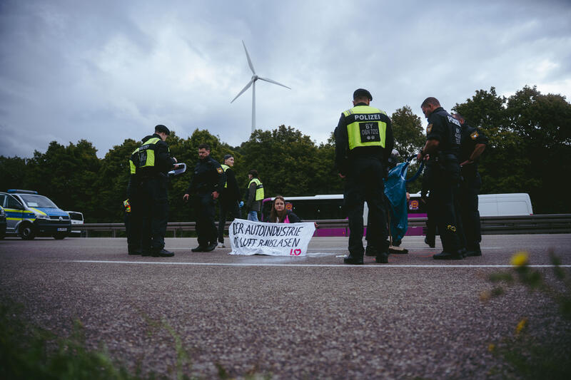 Am 11. September 2025, kurz nach 8, steigen drei Aktivist*innen auf eine Schilderbrücke über der Autobahn nahe der Allianz-Arena in München, Deutschland.
Dazu setzen sich wenig später 6 weitere Aktivist*innen auf die mittlerweile gesperrte Autobahn und kleben sich teilweise fest.
Auch zwei der Aktivist*innen auf der Brücke klebten sich fest, dies verzögerte die Räumung um einiges. Die Aktivist*innen gehörten dem Widerstandskollektiv an und protestierten mit dieser Aktion gegen die IAA, die zurzeit in München stattfindet.  -- On September 11, 2025, shortly after 8 a.m., three activists climb onto a sign bridge above the highway near the Allianz Arena in Munich, Germany.
A little later, six more activists sit down on the now closed highway and partially glue themselves to the ground.
Two of the activists on the bridge also glued themselves to the bridge, which delayed the evacuation considerably. The activists belonged to the resistance collective and were protesting against the IAA, which is currently taking place in Munich.