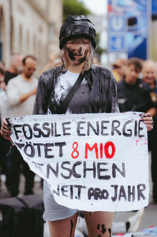 Am 11. September 2025 beteiligten sich um die zwei Dutzend Aktivist*innen an einer Die-In-Aktion von Extinction Rebellion gegen die IAA in München, Deutschland. Dabei legte sich der Großteil auf die Straße und spielte tot. Drei der Aktivist*innen begossen sich mit Mehl, Cola und einem roten Saft, um Staub, Öl und Blut darzustellen. -- On September 11, 2025, around two dozen activists took part in a die-in protest organized by Extinction Rebellion against the IAA in Munich, Germany. Most of them lay down on the street and pretended to be dead. Three of the activists covered themselves in flour, cola, and red juice to represent dust, oil, and blood.