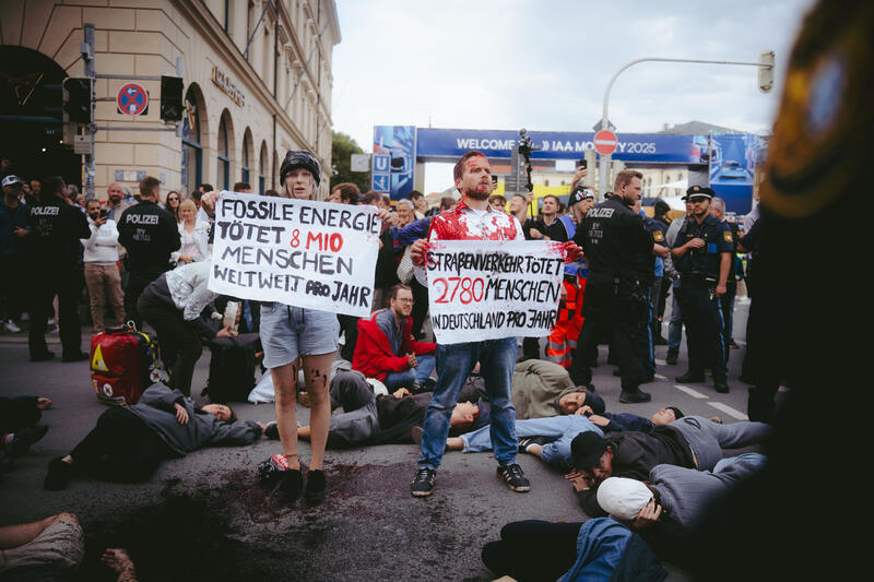 Am 11. September 2025 beteiligten sich um die zwei Dutzend Aktivist*innen an einer Die-In-Aktion von Extinction Rebellion gegen die IAA in München, Deutschland. Dabei legte sich der Großteil auf die Straße und spielte tot. Drei der Aktivist*innen begossen sich mit Mehl, Cola und einem roten Saft, um Staub, Öl und Blut darzustellen. -- On September 11, 2025, around two dozen activists took part in a die-in protest organized by Extinction Rebellion against the IAA in Munich, Germany. Most of them lay down on the street and pretended to be dead. Three of the activists covered themselves in flour, cola, and red juice to represent dust, oil, and blood.