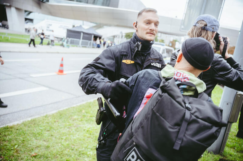 Am 12. September 2025 versammelten sich um die 50 Teilnehmer*innen zu einem Straßenfest gegen die IAA auf einem Grünstreifen vor der BMW-Welt in München, Deutschland. Während der Versammlung kam es immer wieder zu ungehorsamen Aktionen wie dem Besetzen der Straße und dem Klettern auf ein Polizeiauto.  -- On September 12, 2025, around 50 participants gathered for a street party against the IAA on a grass verge in front of BMW Welt in Munich, Germany. During the gathering, there were repeated acts of civil disobedience, such as occupying the street and climbing on a police car.