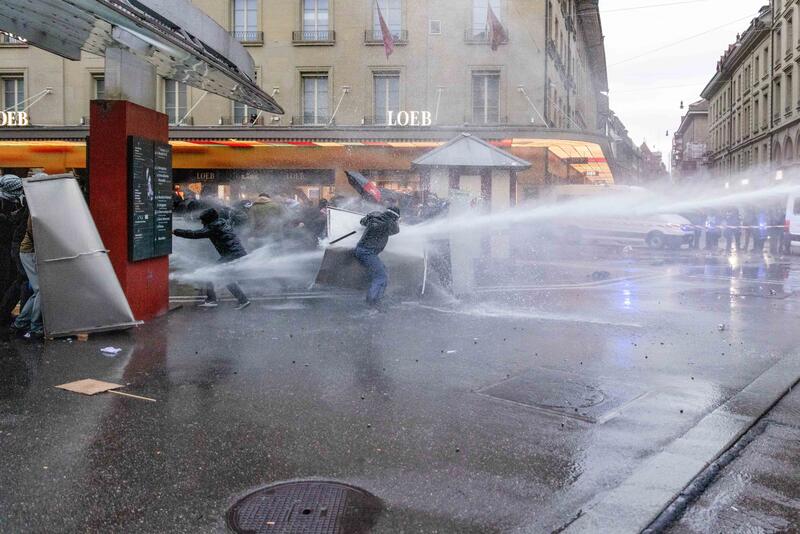 Die Kantonspolizei Bern hält die Demonstrierenden an der Ecke Schauplatzgasse / Bahnhofplatz mit Wasserwerfer und Gummigeschossen in Schach. Die Protestierenden schützen sich mit Blechschildern. Fotografiert am 11. Oktober 2025.    The Bern cantonal police keep the demonstrators at the corner of Schauplatzgasse and Bahnhofplatz in check with water cannons and rubber bullets. The protesters protect themselves with metal signs. Photographed on 11 October 2025.
