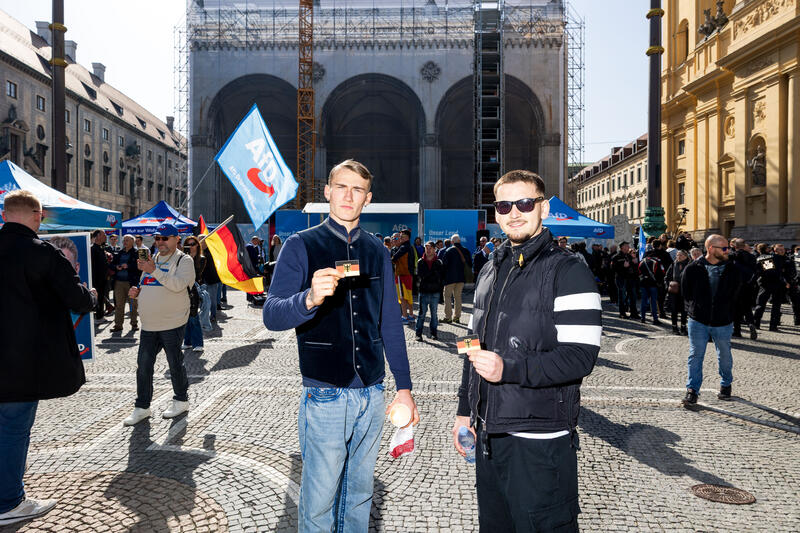 AfD Aktivisten mit Deutschland Flagge als Sticker bei der Kundgebung der AfD Bayern zur Kommunalwahl am 07.03.2026 am Odeonsplatz in München. Drum herum versammelten sich zahlreiche Gegendemonstrant:innen.   --   AfD activists hold Germany flag as sticker at the election campaign rally of the AfD for the municipal elections on March 07, 2026 in Munich, Germany. Several counter-protestors encircled the rally space.