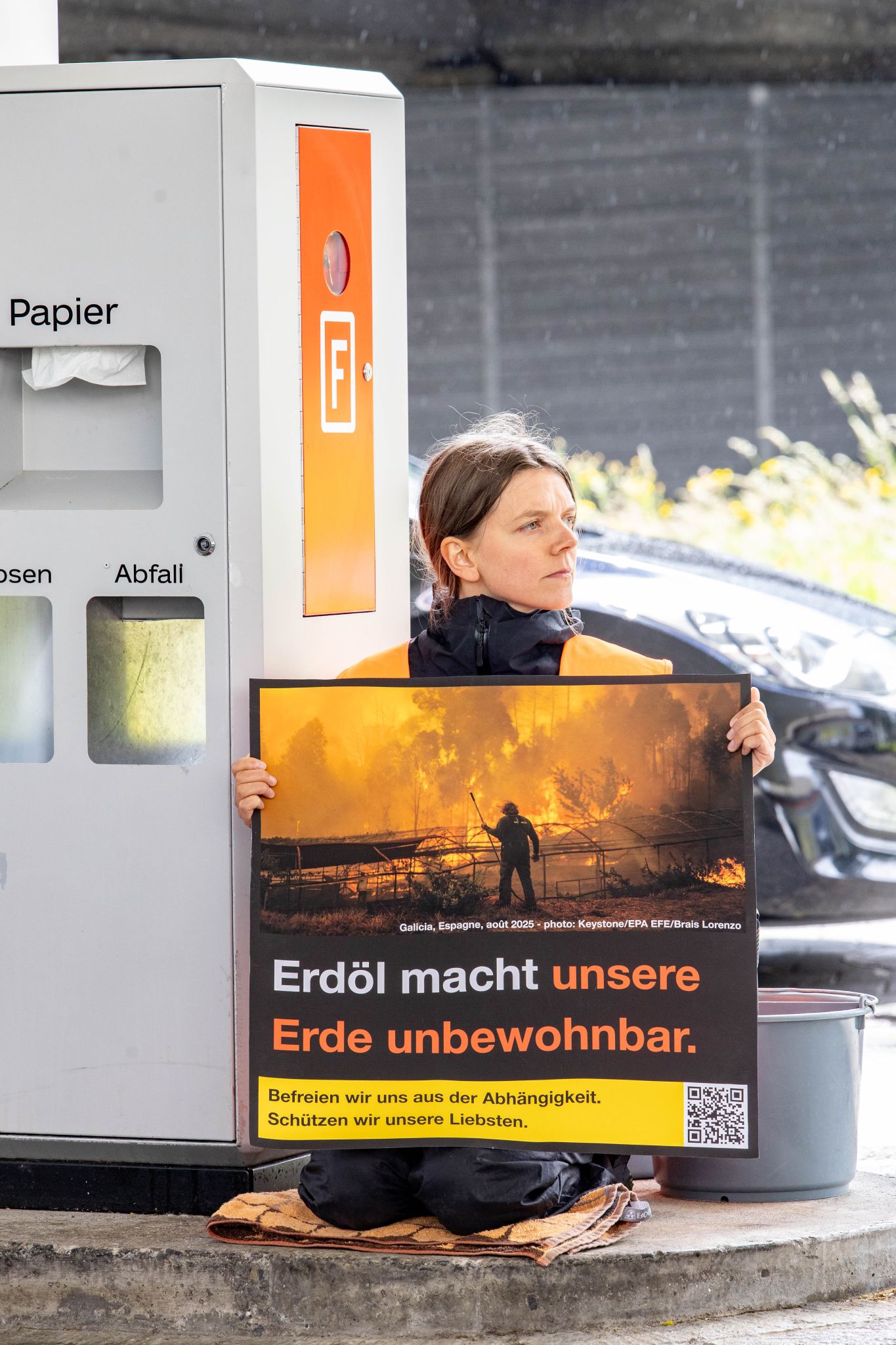 Eine Aktivistin von Act Now sitzt friedlich neben den Zapfsäulen.