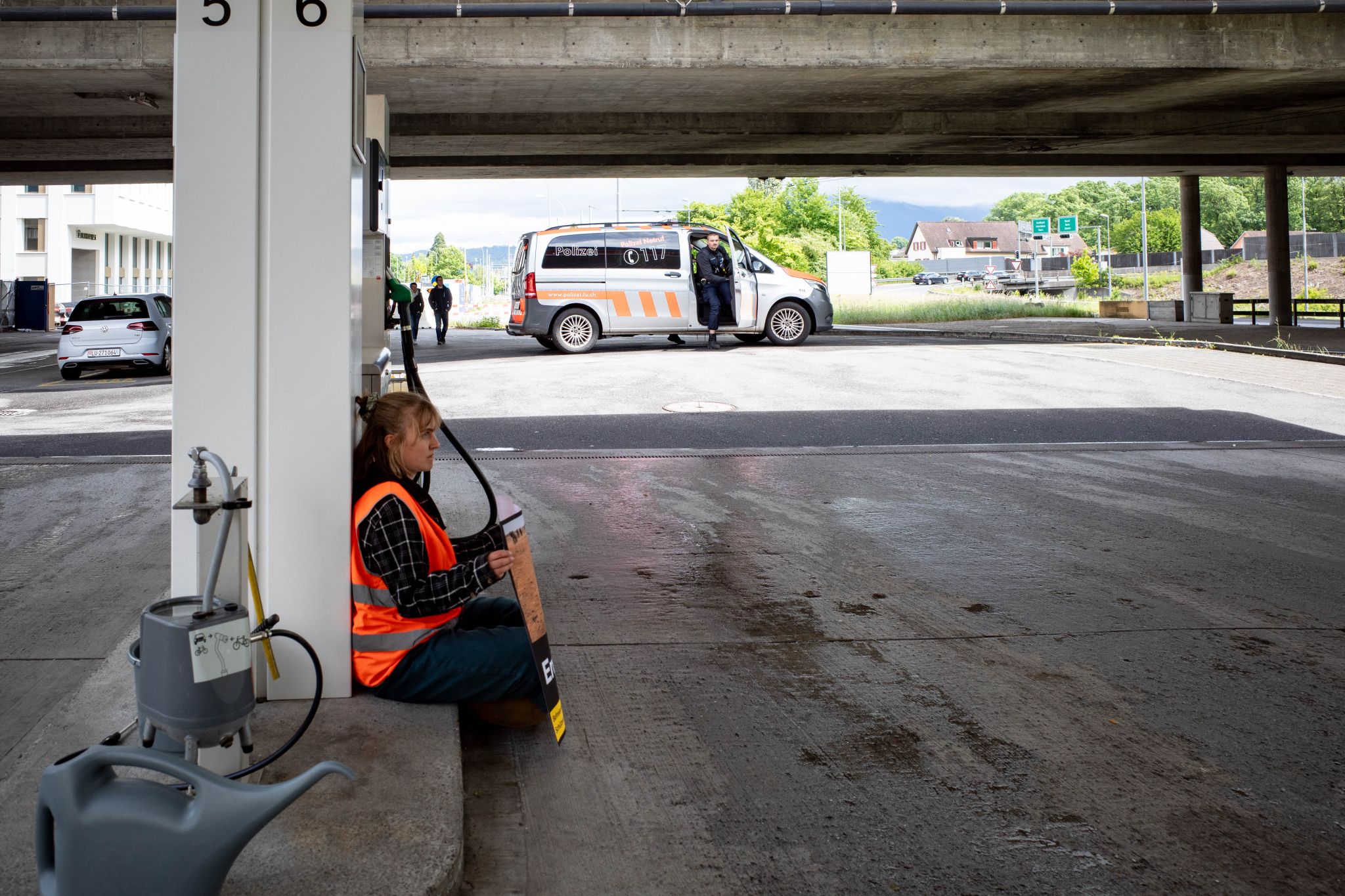 Eine Aktivistin von Act Now sitzt friedlich neben den Zapfsäulen während die Polizei aus dem Einsatzwagen steigt.
