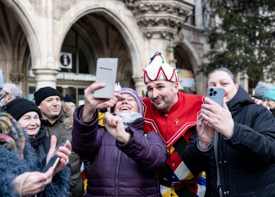 Kasperl und Zuschauerinnen machen beim Schäfflertanz am Marienplatz Selfies.